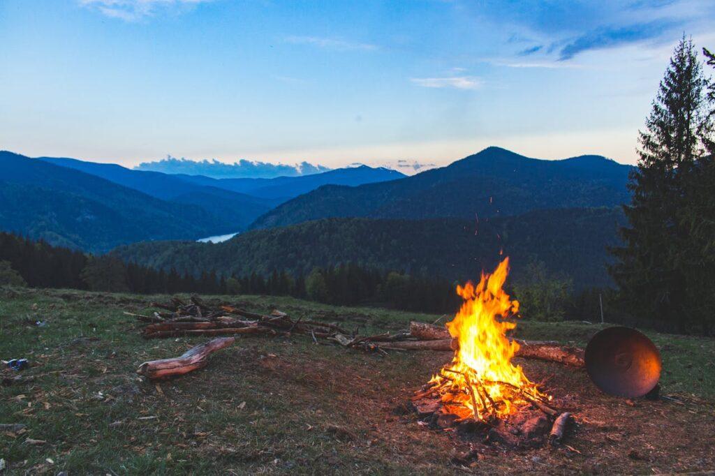 Campfire in den Bergen bei Abenddämmerung, ideal für Reisen mit dem Ford Transit Custom, das Naturerlebnis erweitert.