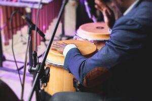 Bongo-Schlagzeuger, der auf einer Bühne mit Conga-Trommeln während einer Jazz-Rock-Show auftritt, mit einer kubanischen Latin-Band im Hintergrund, Blickwinkel des Schlagzeugers