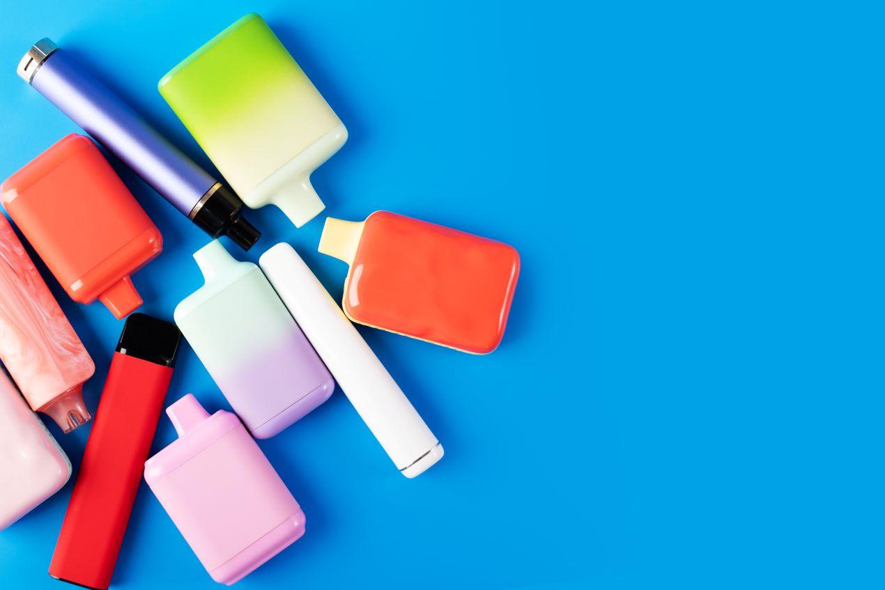 Verschiedene bunte Einweg-E-Zigaretten inklusive Modelle wie die Elf Bar 800 auf blauem Hintergrund